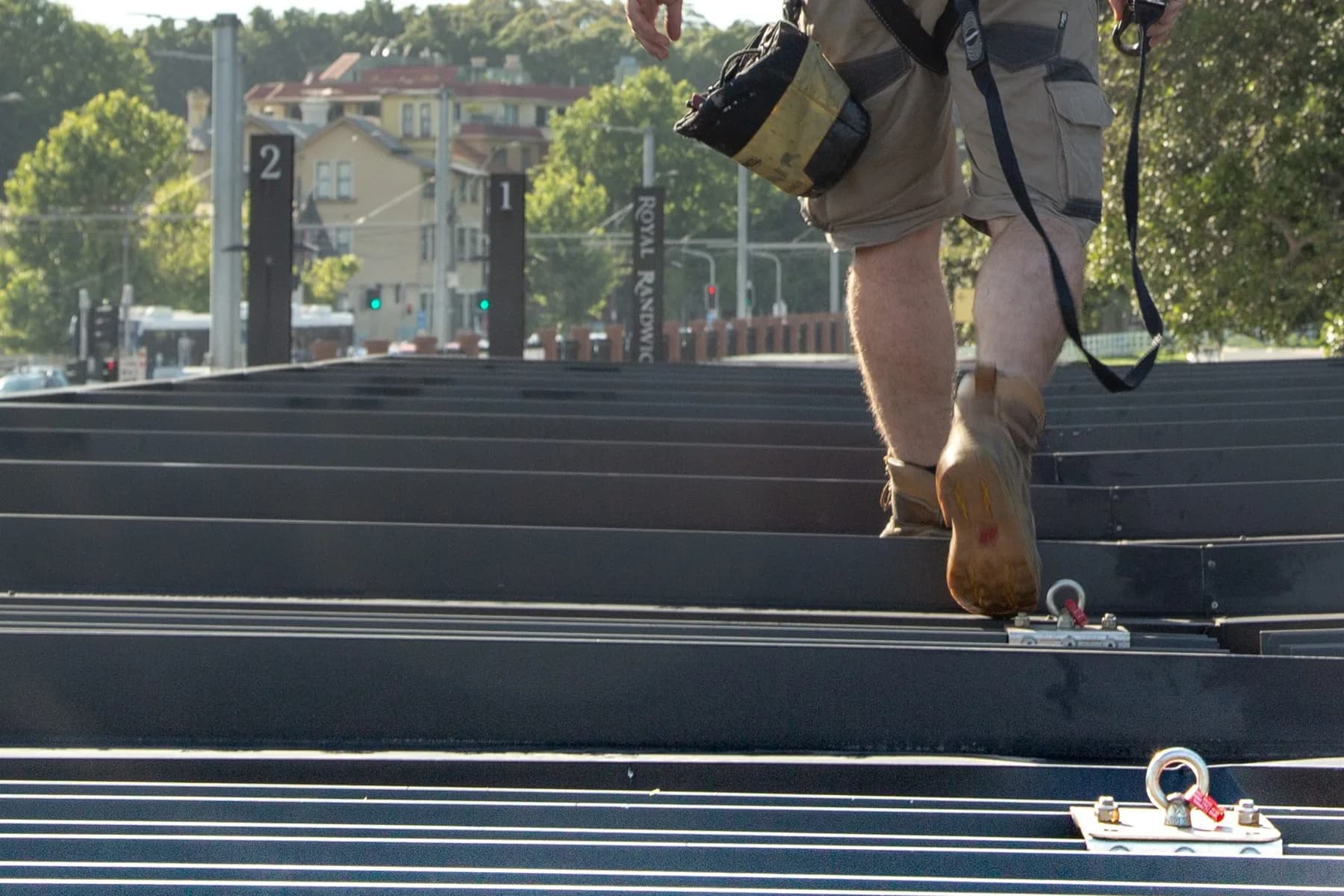 Worker in a harness walking across a metal roof past fixed anchor points