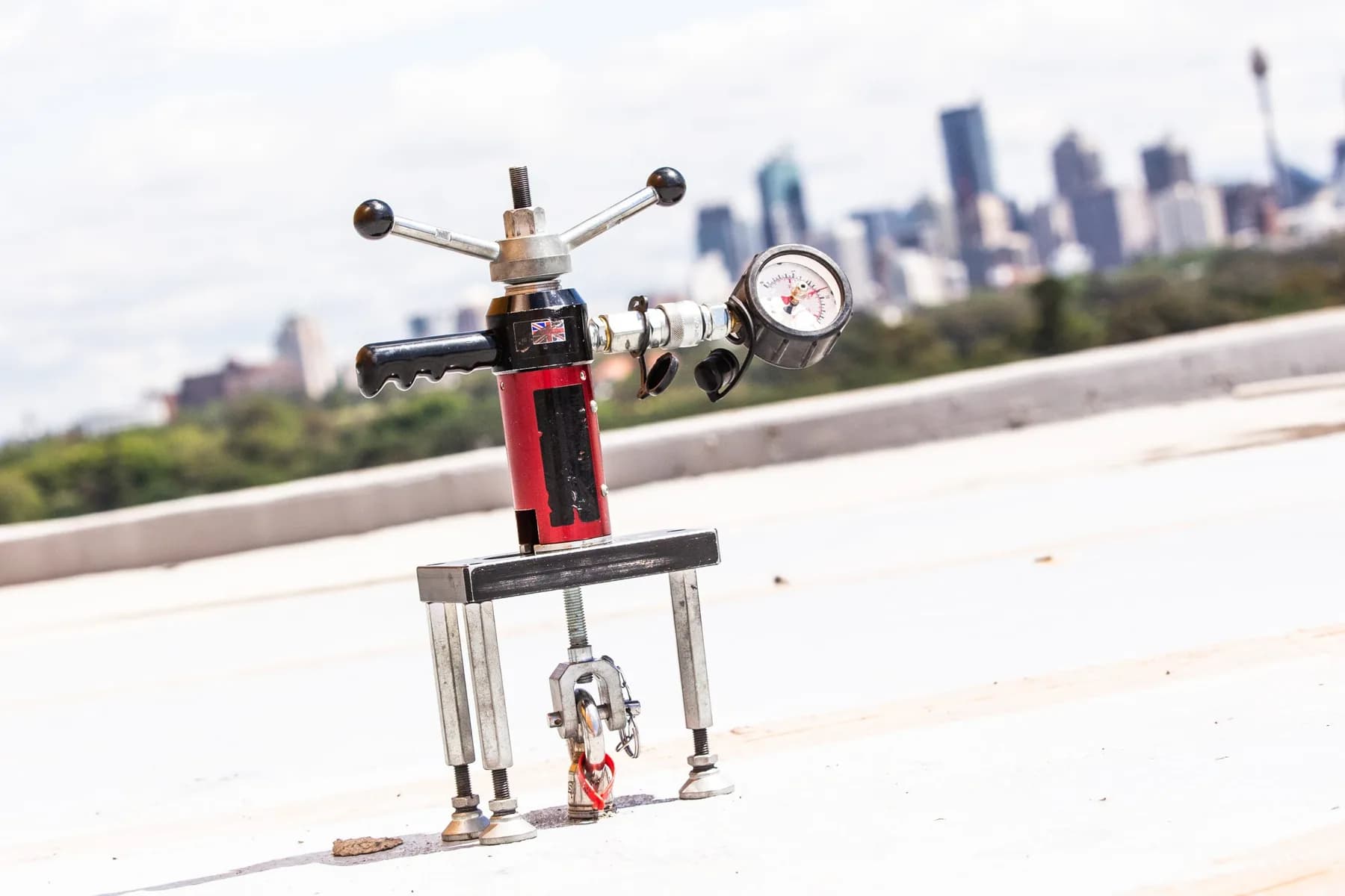 Anchor pull test rig with a pressure gauge set up on a roof, city skyline behind