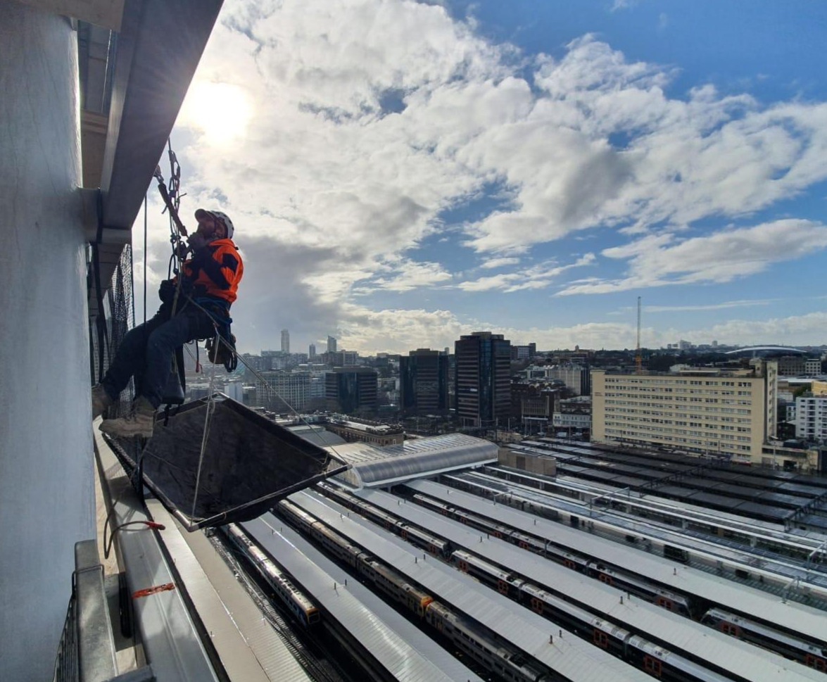 Karabiner rope access technician working on ropes at the edge of a high-rise facade above a Sydney rail yard
