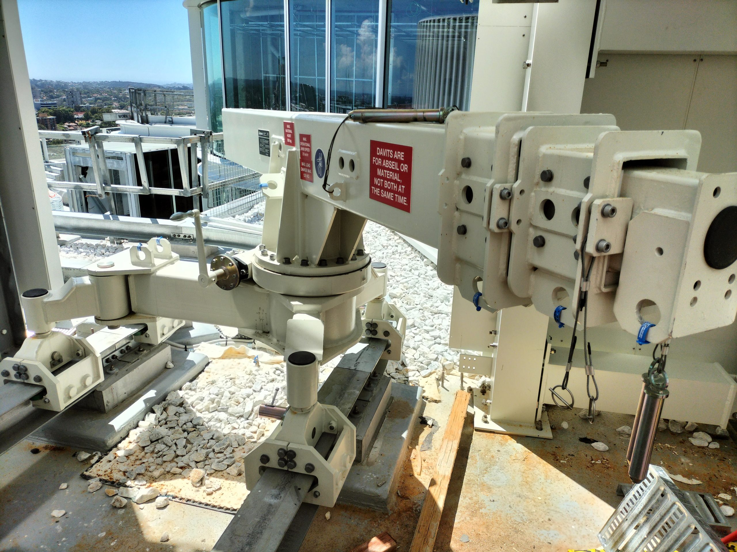 Davit arm installed on a rooftop with a warning label, used for rigging rope access and materials