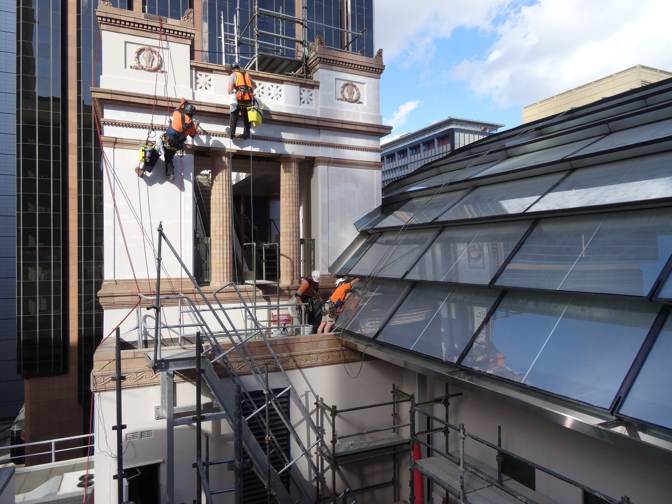Rope access technicians working on a heritage facade in Sydney, with scaffold and stairs set up on the lower roof