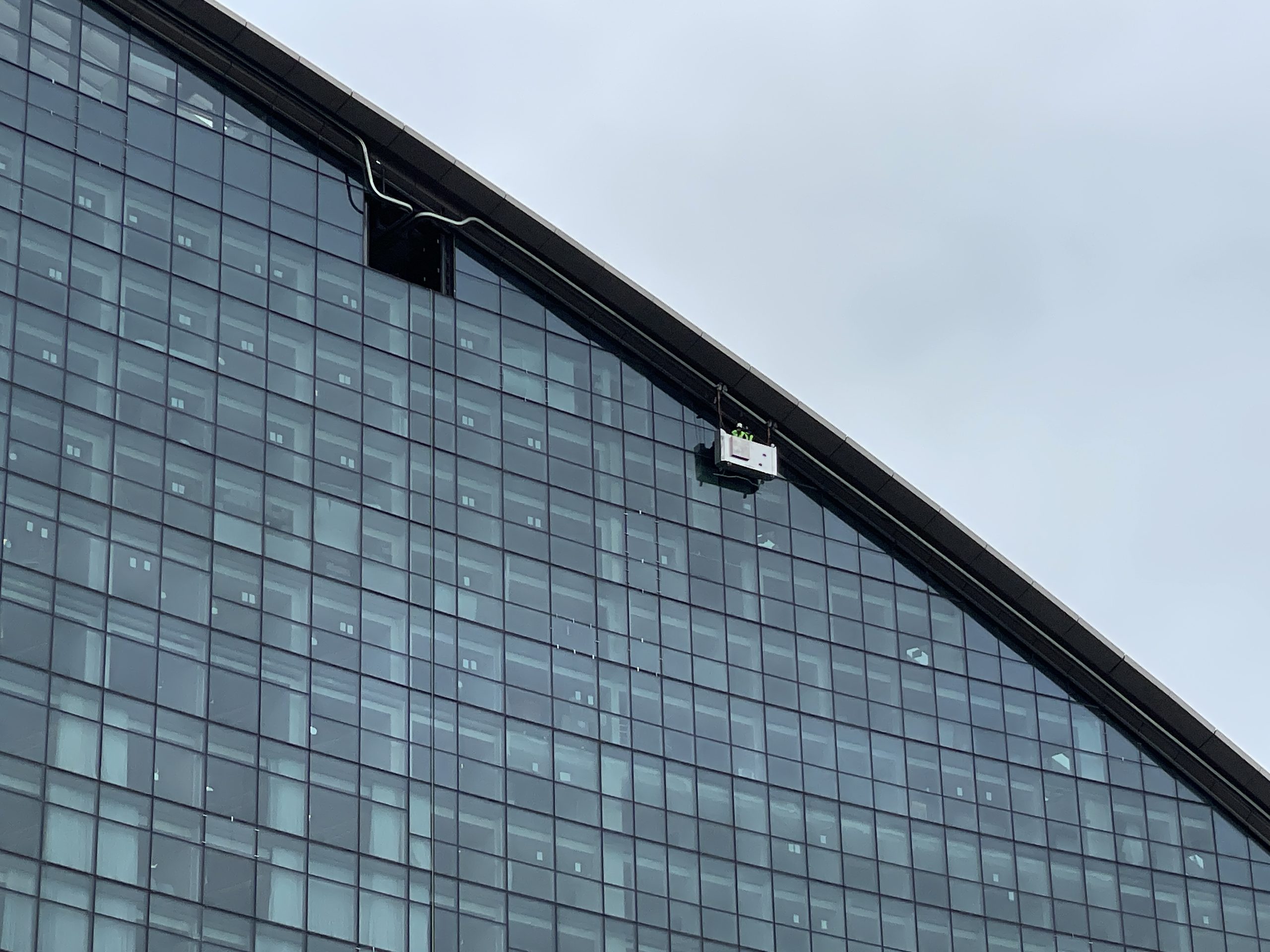 Building maintenance unit cradle with a technician working down the raked glass facade of The Ribbon at Darling Harbour