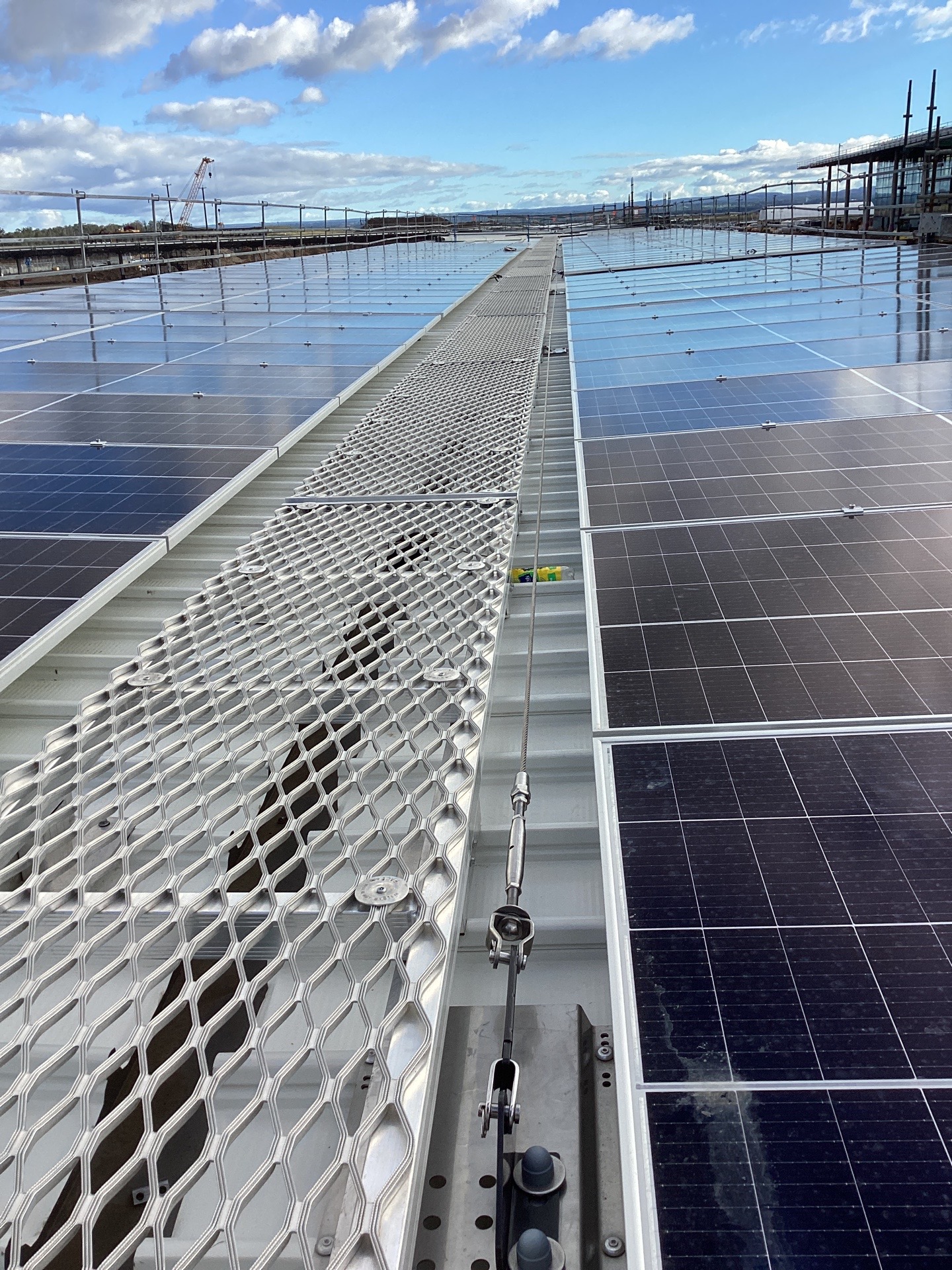 Static line and steel mesh walkway running between rows of solar panels on a roof at Western Sydney International Airport