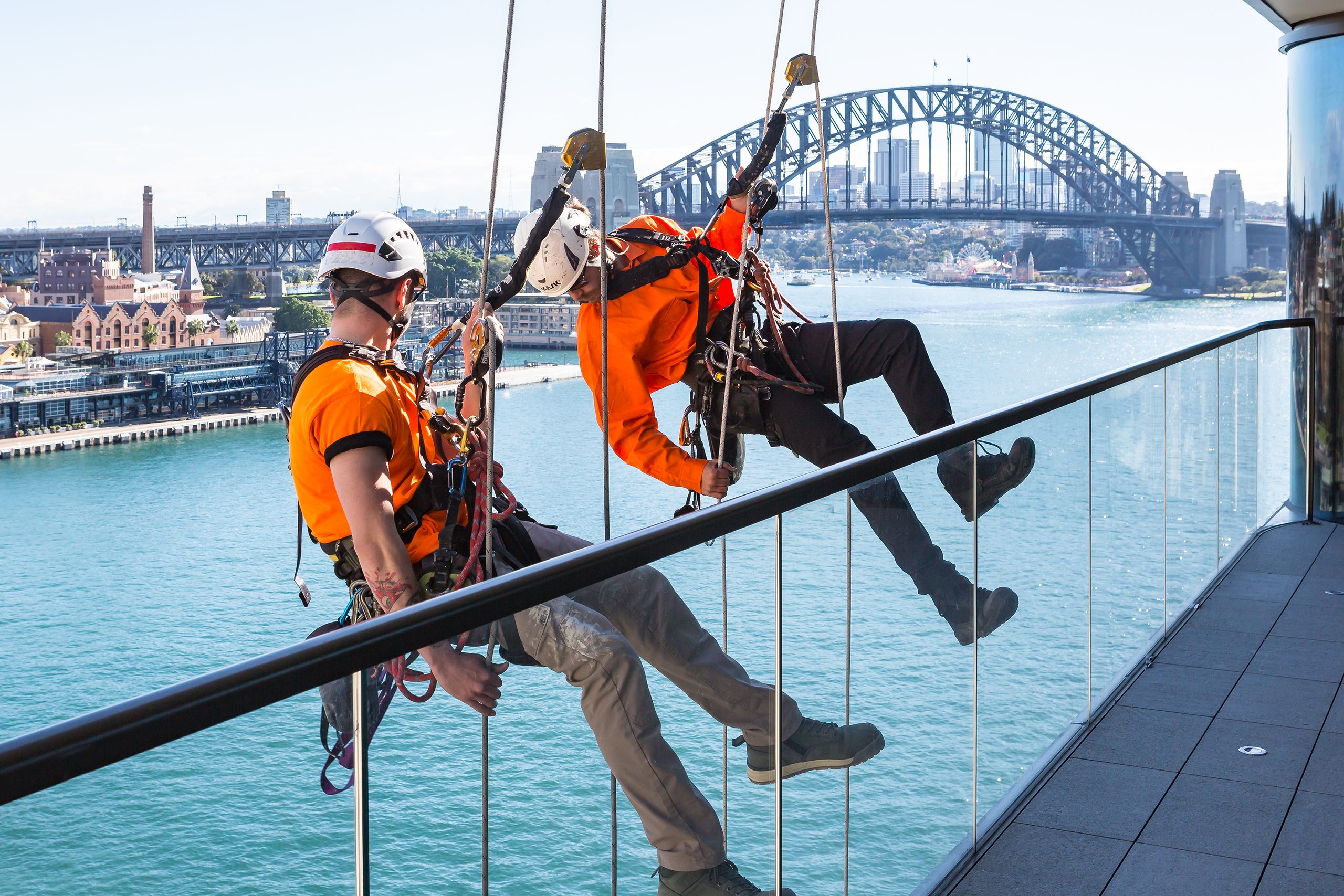 Rope access technician in a harness suspended on twin ropes beside the glazed facade of a Sydney commercial tower